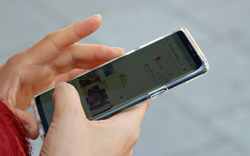 Eine Person hält ein Smartphone in der Hand, das eine Kartenanwendung anzeigt, auf deren Bildschirm Standortpins zu sehen sind.