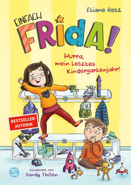 Das Buchcover von "Einfach Frida! Hurra, mein letztes Kindergartenjahr!" zeigt ein fröhliches Mädchen auf einer Bank stehend und einen Jungen sitzend, umgeben von Spielzeug und Schuhen in einer Garderobe.