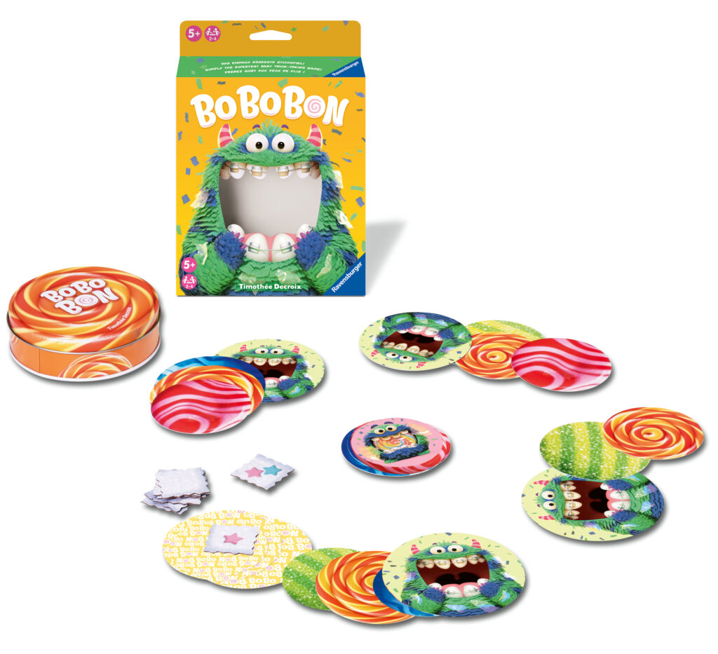 Die Komponenten des BoBoBon-Brettspiels umfassen eine Schachtel, eine runde Dose, bunte kreisförmige Karten mit Monstergesichtern und Bonbonmotiven sowie kleine sternförmige Spielsteine auf weißem Hintergrund.
