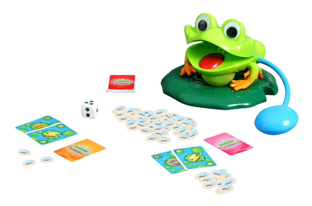 Ein Brettspiel zum Thema Frosch mit einem grünen Plastikfrosch, Karten, Spielsteinen, einem weißen Würfel und einer blauen Luftpumpe, alles auf einer weißen Fläche angeordnet.