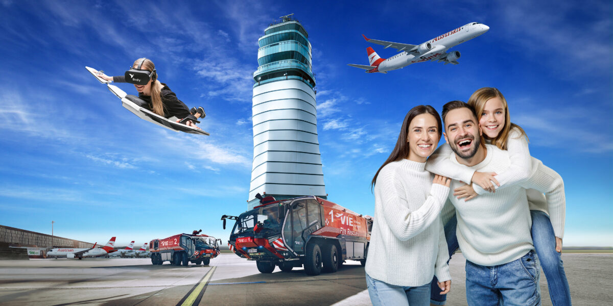 Ein Paar posiert auf einem Flughafen vor einem Kontrollturm, Feuerwehrautos, Flugzeugen und einer Person, die auf einem Jet-Surfbrett am Himmel schwebt.
