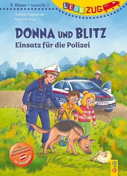Ein Polizeibeamter mit einem Hund unterhält sich mit zwei Kindern vor einem Polizeiauto auf einer Rasenfläche; ein drittes Kind schaut im Hintergrund zu.