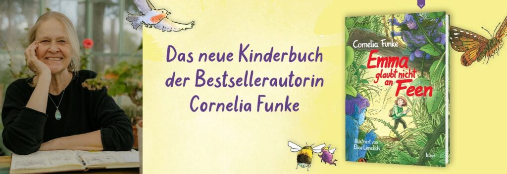 Cornelia Funke sitzt lächelnd an einem Schreibtisch am Fenster, neben einem Plakat, das für ihr neues Kinderbuch „Emma glaubt nicht an Feen“ wirbt.